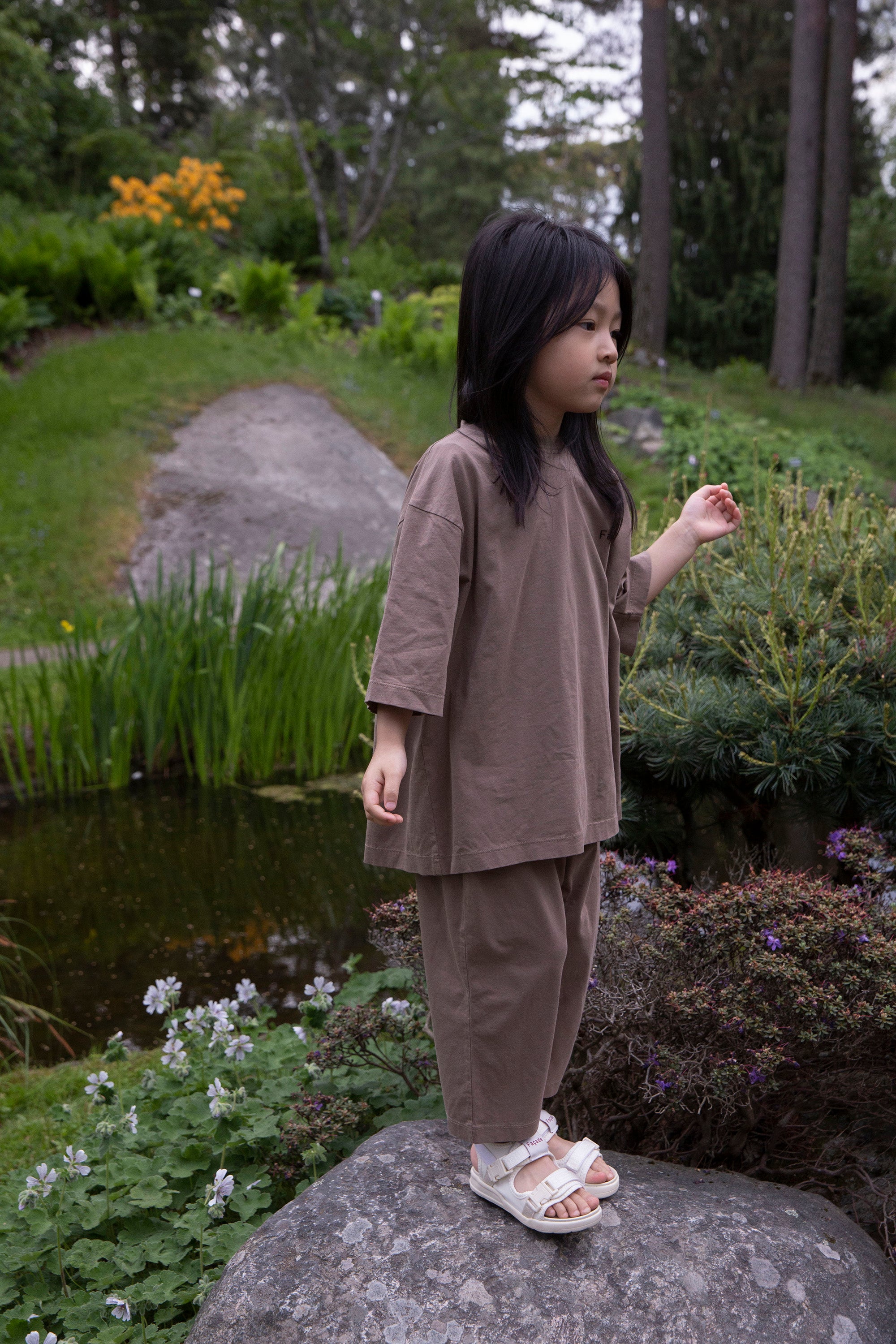 Façade Bato Wide Tee and Kohi Wide Pants in mole, worn by a child, outdoor in a park near the pond