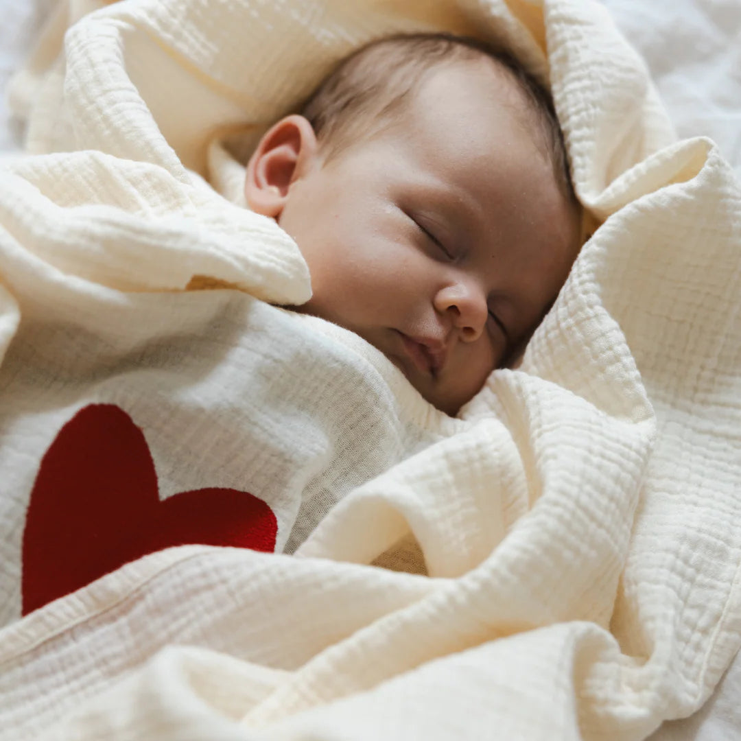 Baby wrapped in 120x120 organic muslin giant swaddle in Cozy White with L’Amour heart detail