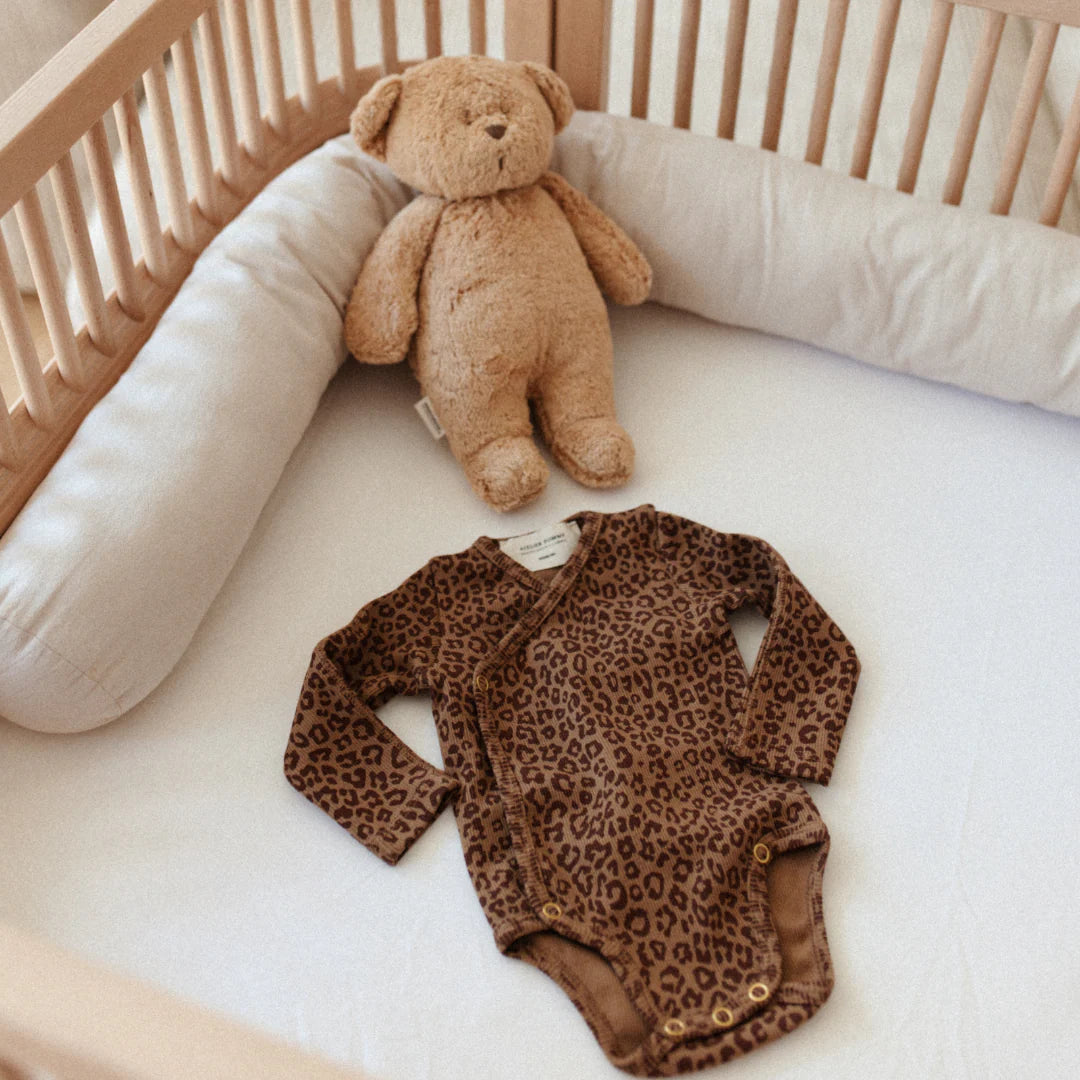 Organic cotton wrap baby bodysuit in leopard print by Atelier Pomme, laid in cot