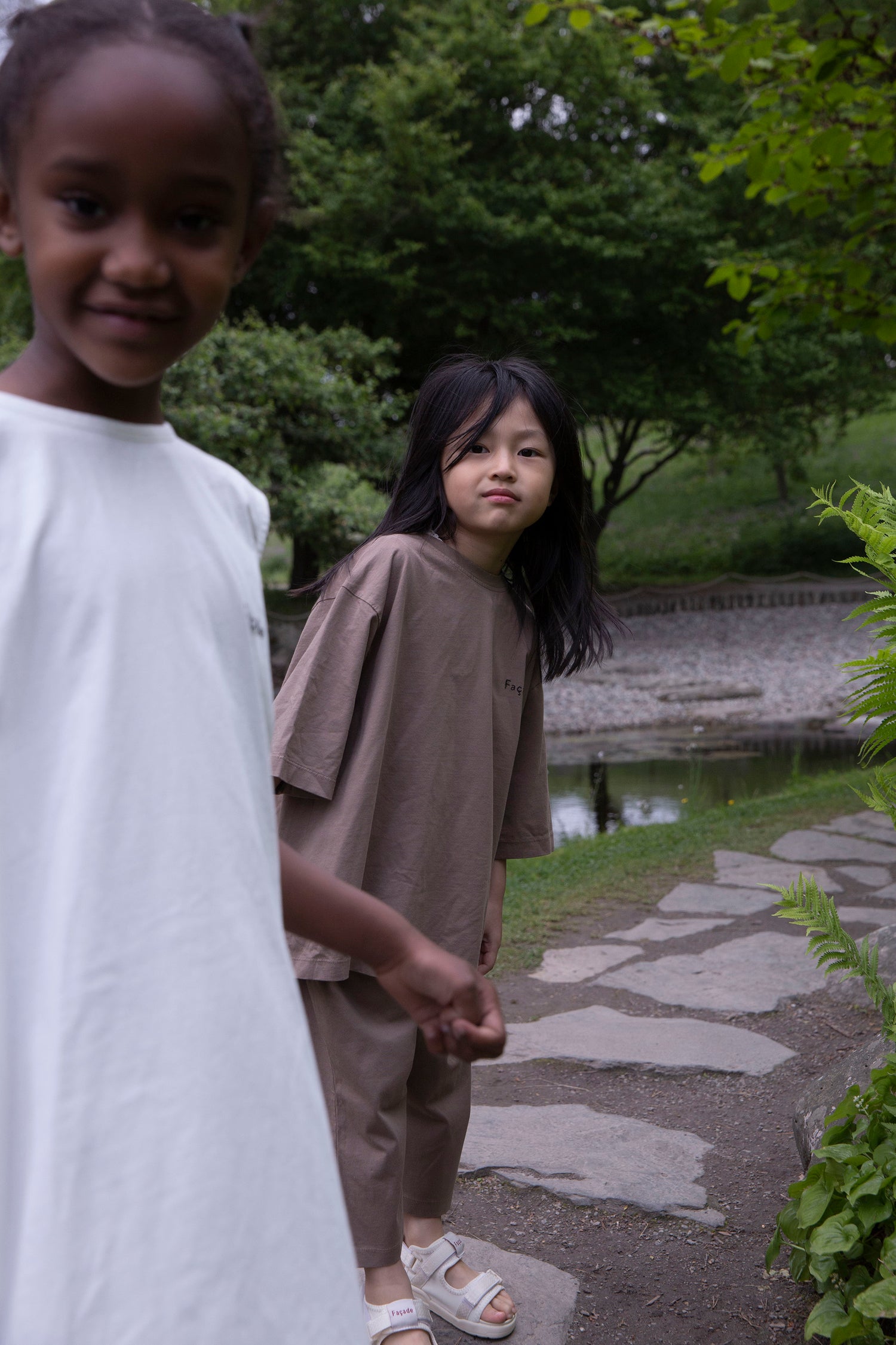 Children wearing Façade Bato Wide Tee and Kohi Wide Pants in mole, organic cotton oversized kids clothing, photographed outdoors in a park