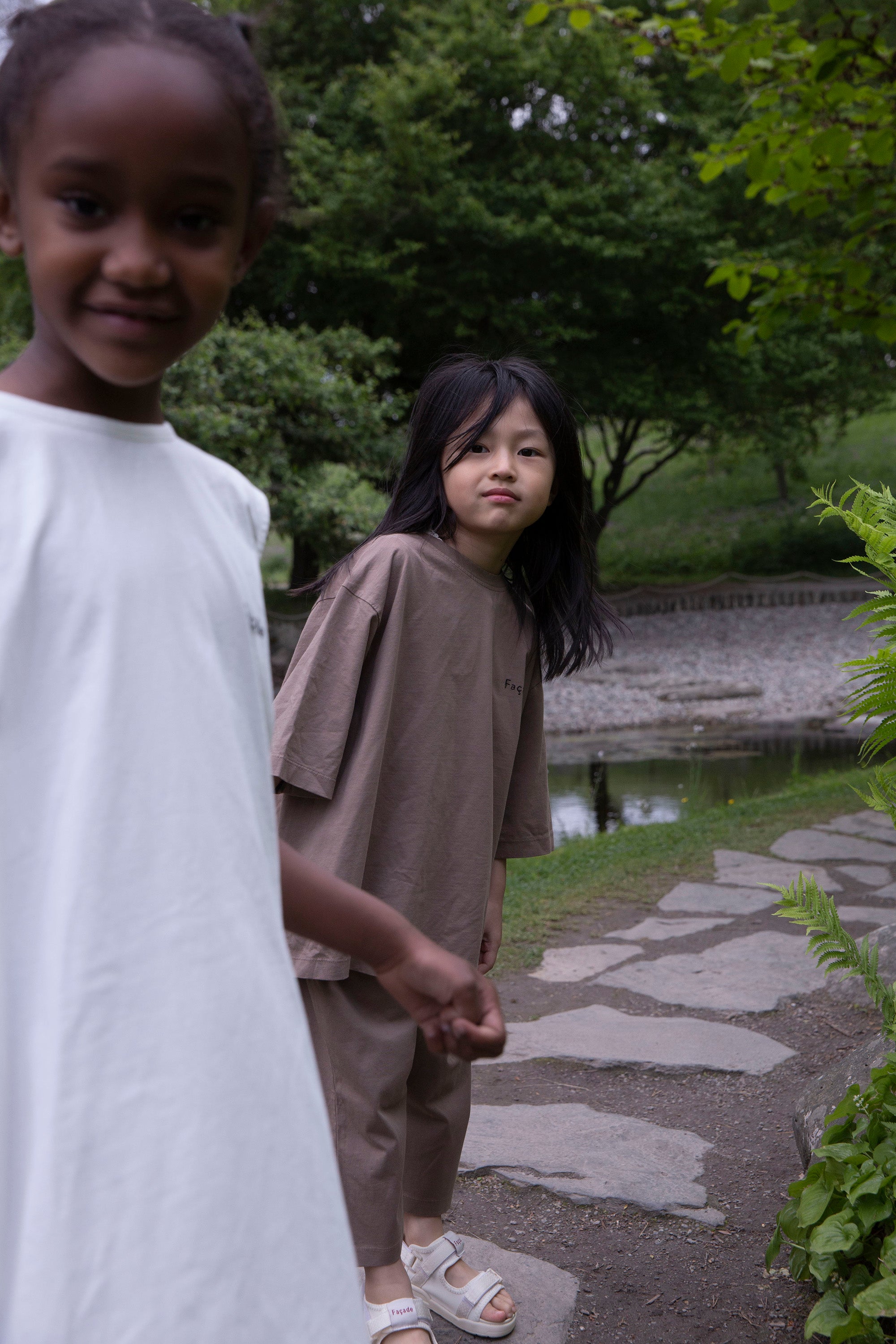 Children wearing Façade Bato Wide Tee and Kohi Wide Pants in mole, organic cotton oversized kids clothing, photographed outdoors in a park