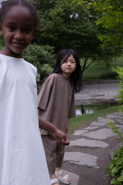 Children wearing Façade Bato Wide Tee and Kohi Wide Pants in mole, organic cotton oversized kids clothing, photographed outdoors in a park
