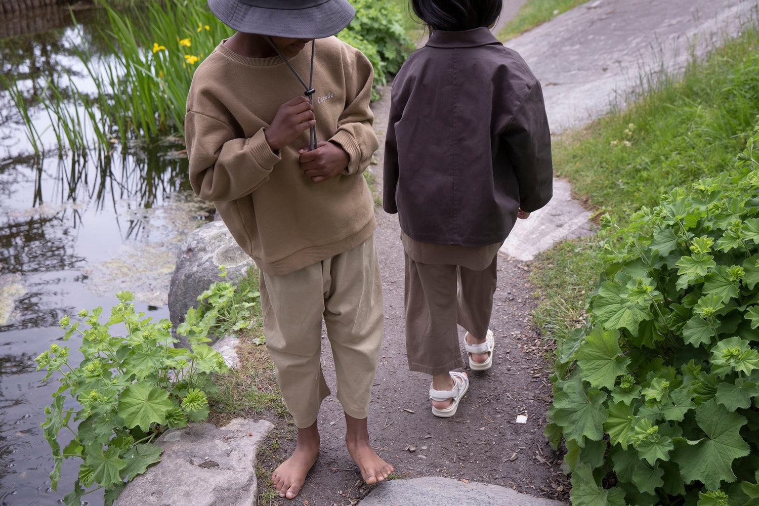 Children wearing Façade Kohi Wide Pants in hay, organic cotton kids trousers with a relaxed barrel fit, photographed outdoors by the water