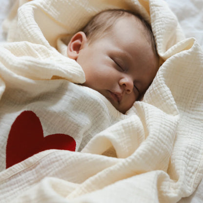 Baby wrapped in 120x120 organic muslin giant swaddle in Cozy White with L’Amour heart detail