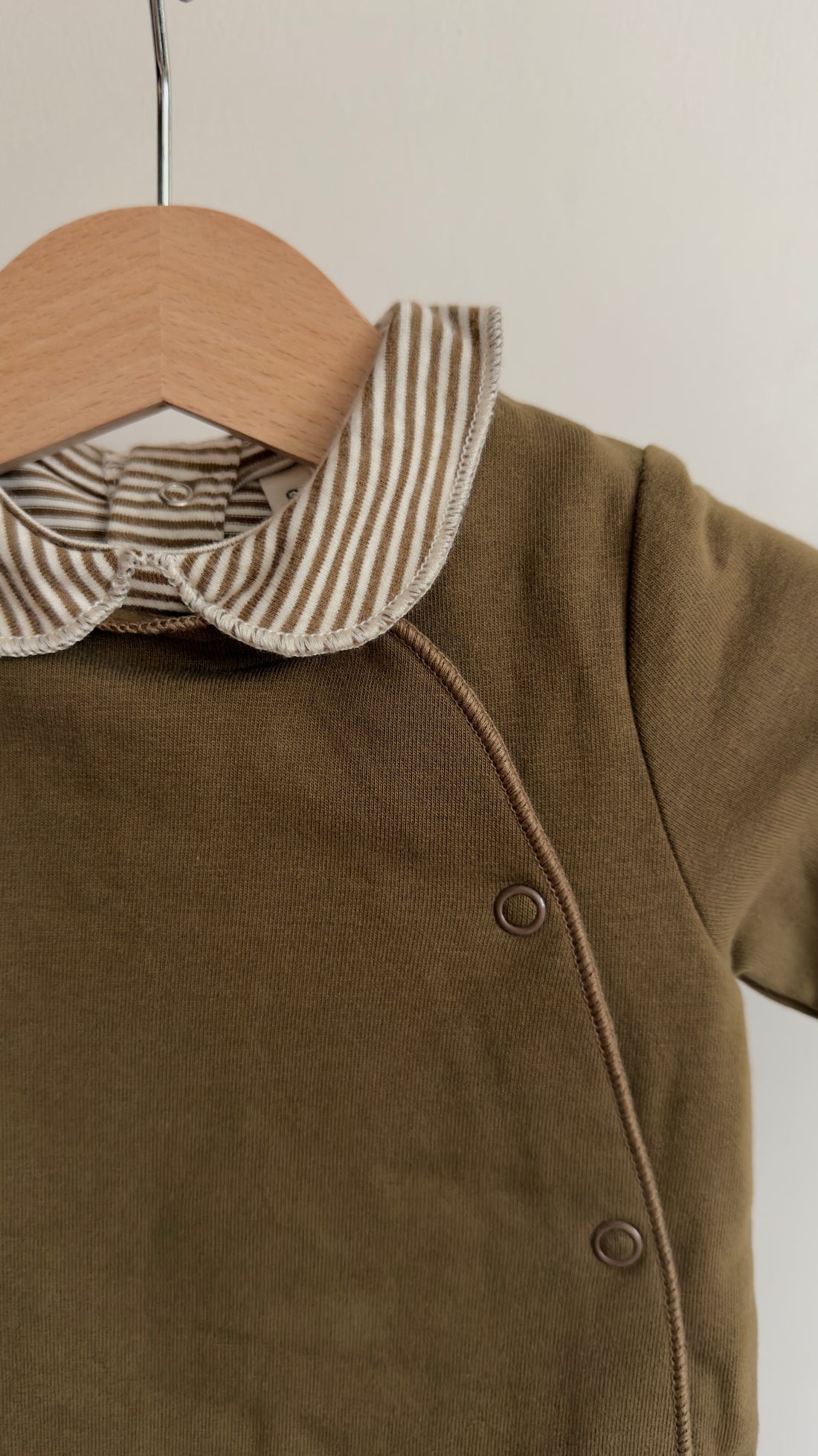 Brown baby outfit with striped collar on a hanger against a neutral background