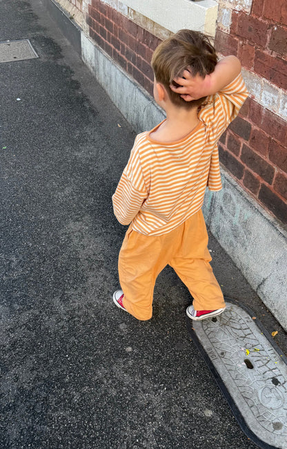 Child wearing Gray Label organic cotton pull up trousers and dropped shoulder tee in melon