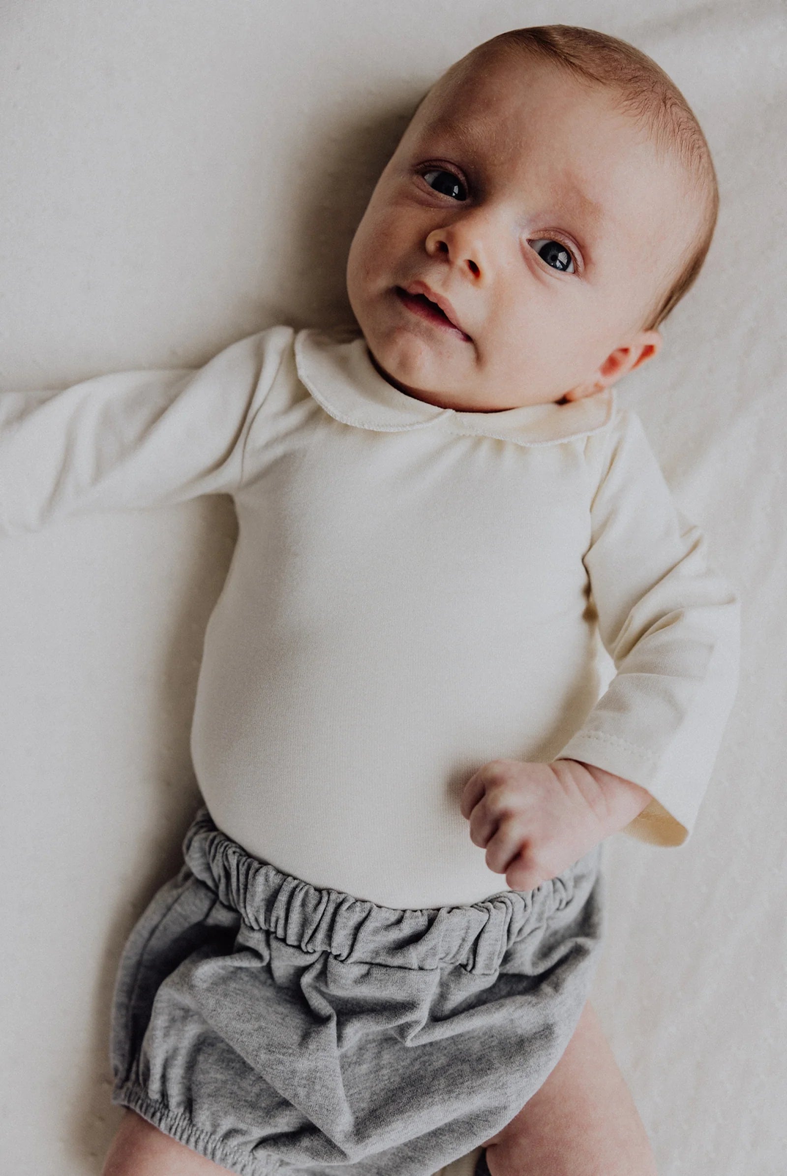 Baby wearing  Gray Label cotton baby collar onesie in cream 