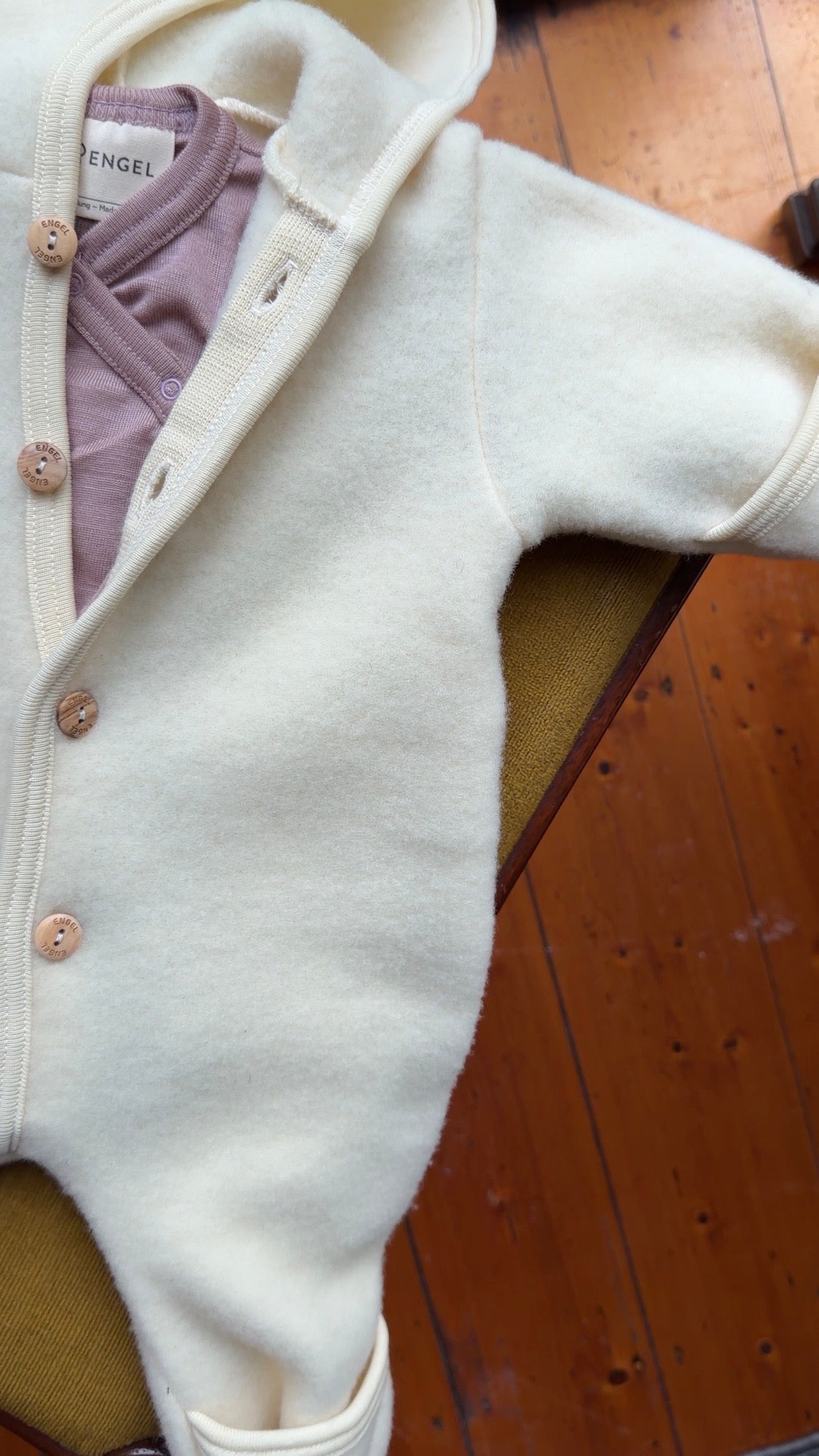 Engel Natur wool fleece overall styled with pink bodysuit laying flat on chair