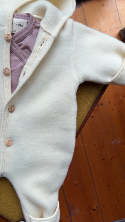 Engel Natur wool fleece overall styled with pink bodysuit laying flat on chair